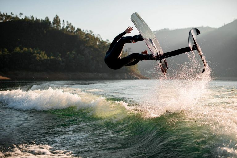 energy athletic man makes extreme stunts jumping and flips on foil wakeboard over splashing wave