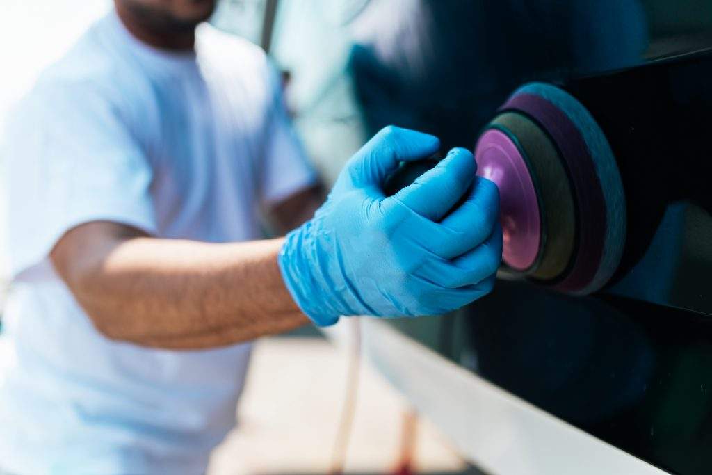 Boat maintenance - Man with orbital polisher polishing boat in marina. Selective focus.